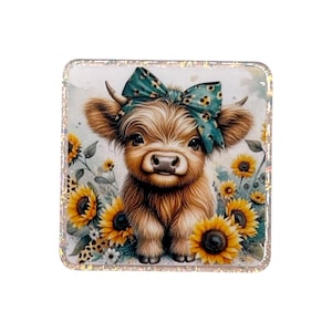 May include: A square coaster featuring a fluffy brown highland cow with a teal bow on its head, surrounded by yellow sunflowers and small white flowers. The coaster has a shimmering, iridescent border that frames the central illustration.