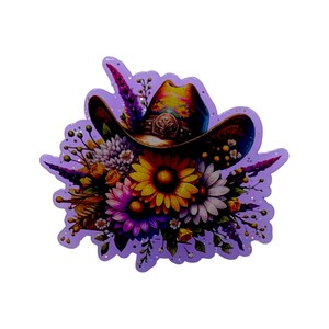 May include: A decorative sticker featuring a cowboy hat adorned with a floral arrangement. The hat is brown with a yellow and blue brim, and the flowers include yellow sunflowers, white daisies, and purple blooms. The sticker has a lavender outline with glitter.