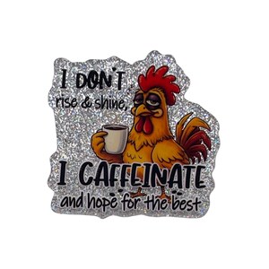May include: A glittery sticker featuring a cartoon rooster holding a coffee cup. The rooster is yellow, orange, and red with a sleepy expression. Text on the sticker reads "I DON'T rise & shine, I CAFFEINATE and hope for the best."