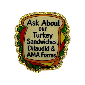 May include: A sandwich-shaped enamel pin with a gold glitter border. The center features a beige bread slice graphic with black text that reads: Ask About our Turkey Sandwiches, Dilaudid & AMA Forms. The design includes red, green, and yellow layers.