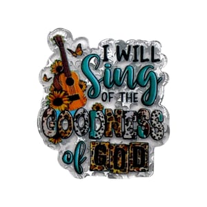 May include: A decorative acrylic piece featuring a brown acoustic guitar, yellow sunflowers, and orange butterflies. The text reads I WILL SING OF THE GOODNESS OF GOD in a mix of teal, black, and leopard print patterns on a clear, textured background.