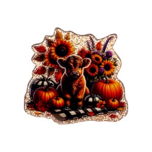 May include: A decorative acrylic pin featuring a fluffy brown Highland calf sitting on a black and white buffalo plaid blanket, surrounded by orange pumpkins, sunflowers, and autumn leaves, all set against a shimmering gold glitter background.