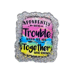 May include: A glitter-edged, rectangular pin with the text "Apparently We're Trouble When We Are Together Who Knew!" in black and yellow. The background features pink, blue, and yellow watercolor-style paint.