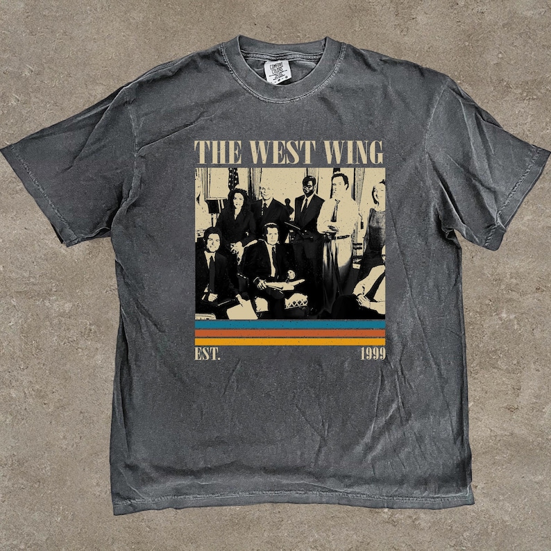 Puede incluir: Camiseta gris oscuro con un dise&ntilde;o gr&aacute;fico de la serie de televisi&oacute;n "El Ala Oeste de la Casa Blanca". El dise&ntilde;o incluye una foto grupal del elenco, el t&iacute;tulo del programa y el a&ntilde;o "1999". La camiseta tiene un aspecto vintage y desgastado.