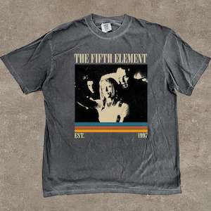 May include: Dark grey t-shirt with a graphic from the film "The Fifth Element". The design features a retro image with the film's title and the year 1997. The shirt has a vintage, worn appearance.