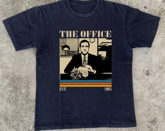 Może przedstawiać: Granatowa koszulka z grafiką Michaela Scotta z The Office. Projekt zawiera logo serialu, napis "EST. 2005" oraz wizerunek Michaela Scotta trzymającego kubek "World's Best Boss". Koszulka ma wygląd vintage.