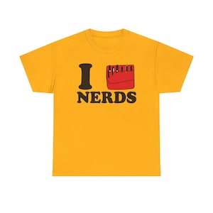 Puede incluir: Camiseta de color amarillo mostaza con la frase "I NERDS" en negro y rojo. La "I" es una letra en negrita de color marrón oscuro, y la palabra "NERDS" está en negrita, con una fuente sans-serif. Un gráfico rojo sigue a la "I".