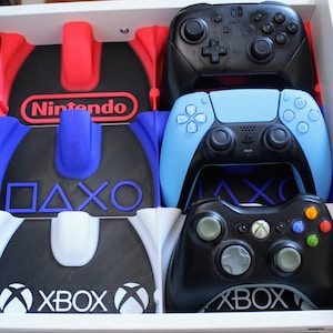 May include: A drawer organiser with sections for video game controllers. The organiser features sections labelled "Nintendo", "PlayStation", and "Xbox". Controllers for Nintendo Switch, PlayStation, and Xbox are visible in the drawer.