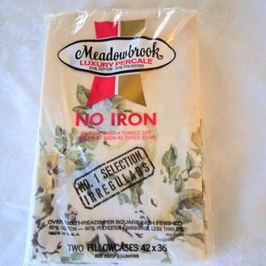 May include: A package of Meadowbrook Luxury Percale pillowcases. The package is clear plastic, and the pillowcases have a floral pattern with green and yellow flowers. The package reads "No Iron" and "Two Pillowcases 42 x 36".