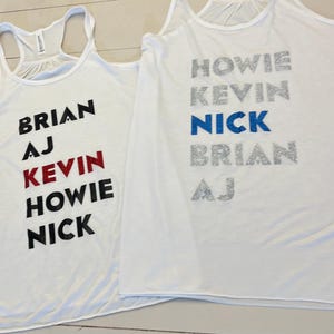 May include: Two white tank tops with names printed on them. The left tank top has the names Brian, AJ, Kevin, Howie, and Nick printed in black, red, and white. The right tank top has the names Howie, Kevin, Nick, Brian, and AJ printed in silver and blue.