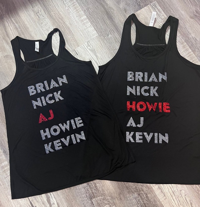 May include: Two black tank tops with silver glitter lettering. The text on the left tank top reads "Brian Nick AJ Howie Kevin". The text on the right tank top reads "Brian Nick Howie AJ Kevin". The word "Howie" is in red glitter on both tank tops.