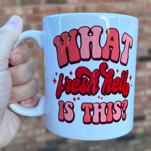May include: White ceramic mug with a red and pink graphic that says "WHAT fresh hell IS THIS?"