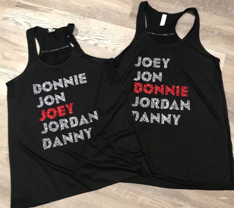 May include: Two black racerback vests with silver and red glitter text. The text on the first vest reads "DONNIE, JON, JOEY, JORDAN, DANNY." The second vest reads "JOEY, JON, DONNIE, JORDAN, DANNY."