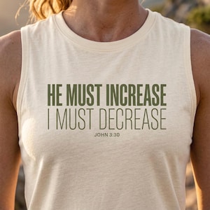May include: Cream-coloured vest top with the text "HE MUST INCREASE I MUST DECREASE JOHN 3:30" in olive green. The sleeveless top is made of a soft, lightweight material.