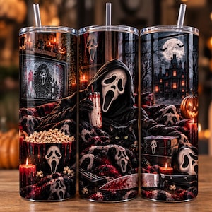 May include: A cylindrical stainless steel tumbler with a clear straw, featuring a dark horror-themed graphic print. The design includes a masked figure, a black cat, a bowl of popcorn, a haunted mansion under a full moon, and red candles.