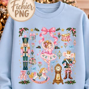 May include: A light blue crewneck sweatshirt featuring a central graphic print of a ballerina, a nutcracker, a mouse soldier, a rocking horse, a grandfather clock, and a pink bow, surrounded by small holiday ornaments, stars, and gift boxes.