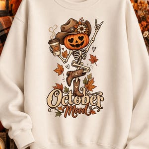 Può includere: Una felpa girocollo color crema con la grafica di uno scheletro con testa di zucca che indossa un cappello da cowboy e stivali. Lo scheletro tiene in mano una tazza di caffè e fa un gesto con la mano, circondato da foglie autunnali e dal testo October Mood.