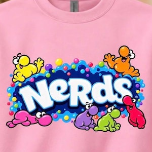 May include: A light pink crewneck sweatshirt featuring a colorful graphic print of the word NERDS in white letters. The design includes several small, cartoonish, multi-colored characters in yellow, orange, pink, purple, green, and red.