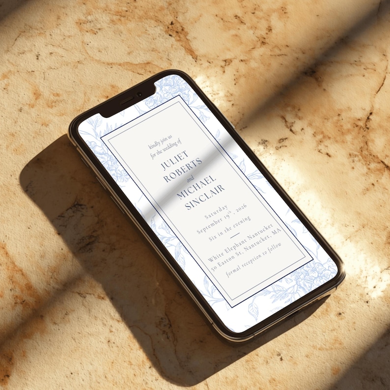 May include: A smartphone displays a wedding invitation. The invitation features the names Juliet Roberts and Michael Sinclair, with the date September 19, 2016, and the venue, White Elephant Nantucket. The design includes floral accents in light blue.
