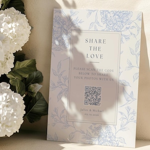 May include: A rectangular sign featuring a light blue floral and bird pattern on a white background. The center text reads SHARE THE LOVE, PLEASE SCAN THE CODE BELOW TO SHARE YOUR PHOTOS WITH US, a QR code, Juliet & Michael, and 09.19.2026.