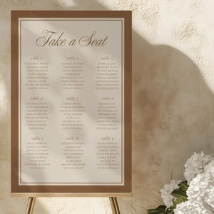 Puede incluir: Un cartel rectangular de distribución de asientos para bodas con borde marrón y centro beige. El texto "Take a Seat" está impreso en una fuente cursiva marrón en la parte superior, seguido de nueve mesas con nombres en fuente serif marrón.