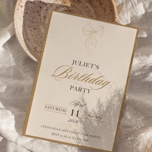 以下が含まれることがあります： クリーム色の誕生日パーティーの招待状。金色の文字とリボンのイラストが特徴です。「Juliet's Birthday Party」と書かれており、日付は「2026年4月11日」、時間は「午後8時」です。招待状にはRSVP情報も含まれています。