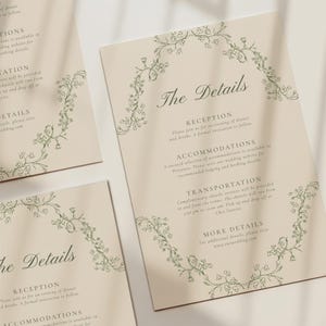 Peut inclure: Cartes de détails de mariage crème avec des bordures florales vertes. Les cartes présentent le texte "The Details" et incluent des informations sur la réception, l'hébergement et le transport. Les cartes sont disposées sur une surface blanche.
