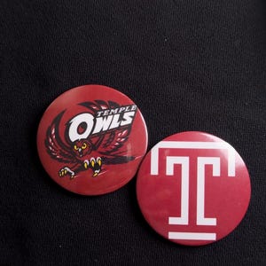 May include: Two circular pin-back buttons with a cherry red background. One button features a graphic of an owl with the text Temple Owls. The other button displays a large white letter T with a horizontal bar above and below the letter.