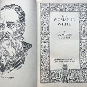 May include: An open book with a black and white illustration of a man with a beard and glasses on the left page. The right page displays the title "THE WOMAN IN WHITE" by W. Wilkie Collins.