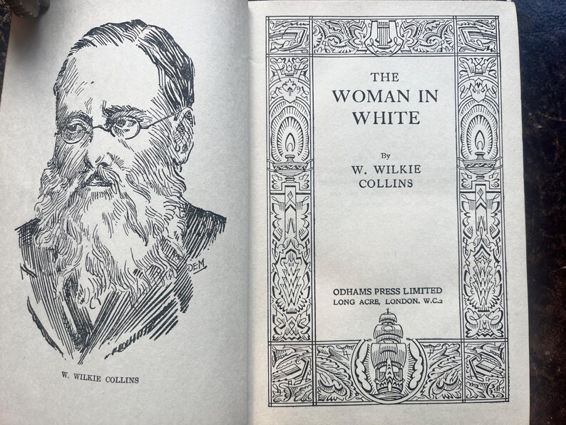 May include: An open book with a black and white illustration of a man with a beard and glasses on the left page. The right page displays the title "THE WOMAN IN WHITE" by W. Wilkie Collins.