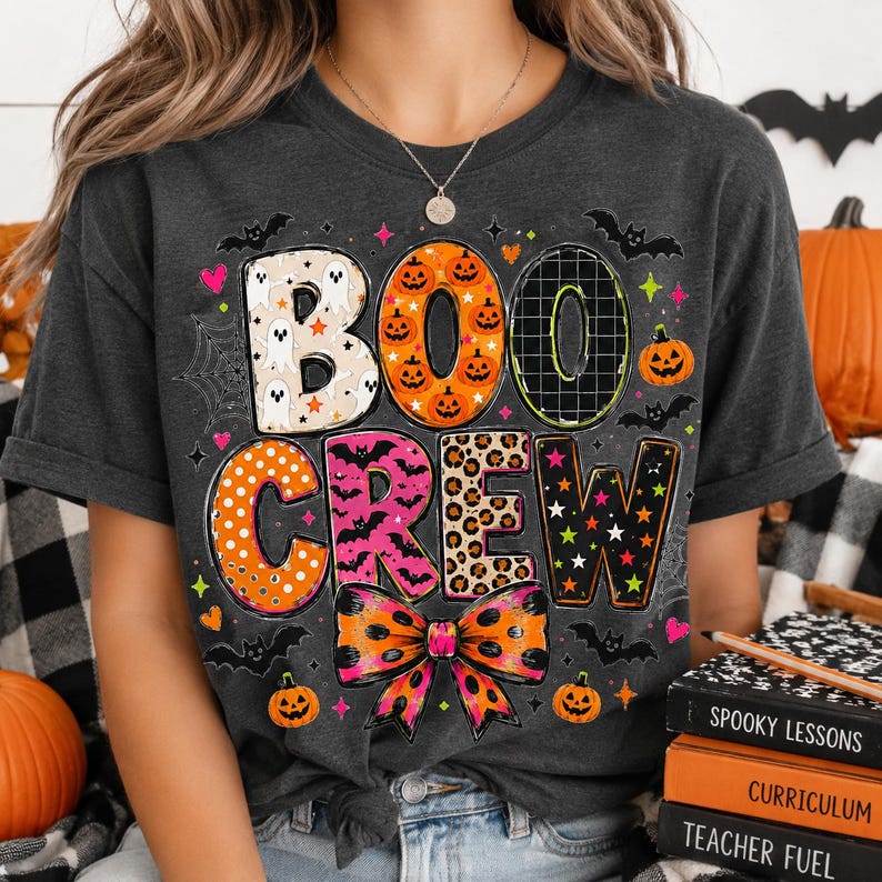 A person wearing a black t-shirt with a Halloween-themed design, including the text "BOO CREW" and various Halloween-related elements such as bats, pumpkins, and a leopard print bow.