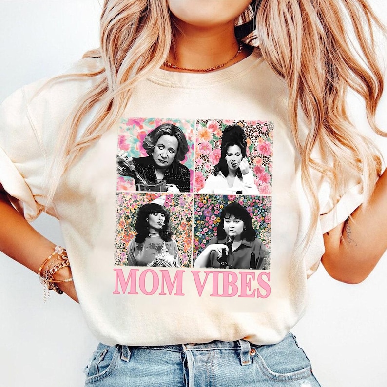 A woman wearing a white t-shirt with a collage of four images of women, along with the text "MOM VIBES" printed on it.