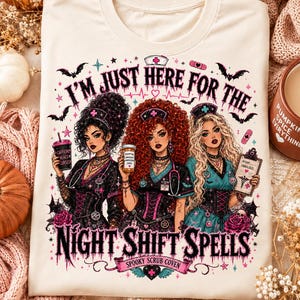 May include: A cream-colored t-shirt featuring a graphic of three nurses with distinct hairstyles, wearing dark scrubs and nurse caps. The text reads I'M JUST HERE FOR THE NIGHT SHIFT SPELLS and SPOOKY SCRUB COVEN, surrounded by bats, stars, and medical icons.