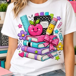 A white t-shirt with a colorful graphic design depicting a stack of books, a pencil, an apple, and various other school supplies.