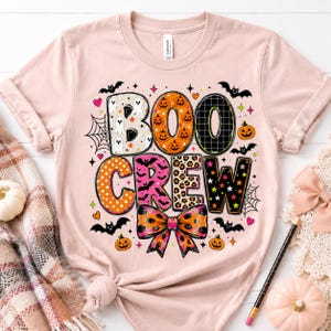 A pink t-shirt with a Halloween-themed design, including the text "BOO CREEK" and various decorative elements such as bats, pumpkins, and a bow.