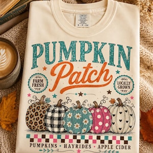 May include: A cream-colored t-shirt featuring the text PUMPKIN PATCH, FARM FRESH, LOCALLY GROWN, PUMPKINS, HAYRIDES, and APPLE CIDER. The graphic includes five pumpkins with leopard, buffalo plaid, daisy, polka dot, and heart patterns.