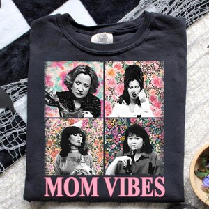 The image is a t-shirt with a collage of four black and white photographs of women, each with a different expression. The text "MOM VIBES" is printed below the collage.