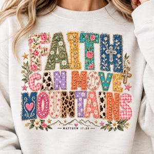 Puede incluir: Una sudadera de cuello redondo de color claro con el texto FAITH CAN MOVE MOUNTAINS en grandes letras de bloque con varios patrones. El diseño incluye estampados florales, de leopardo, cuadros y mezclilla con cruces, estrellas y Matthew 17:20.
