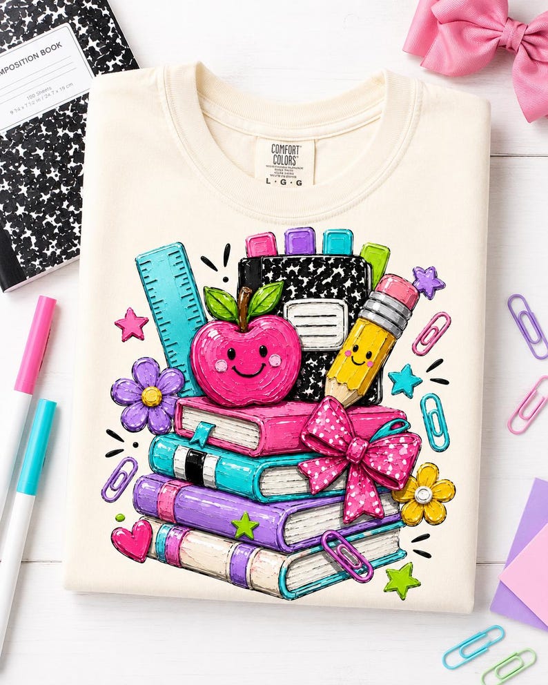 a white t-shirt with a colorful illustration of school supplies, including a pencil, a book, and a flower, along with a smiling apple. The t-shirt is surrounded by various school supplies, such as markers, scissors, and a notebook, creating a playful and educational atmosphere.