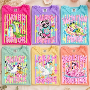 Puede incluir: Una colección de camisetas coloridas con gráficos y texto divertidos. Los diseños incluyen un caimán con el texto "Later Gator", un mapache con "Messy Bestie" y una rana con "Vacation Mode". Otras camisetas presentan una gaviota, un ganso y un flamenco.