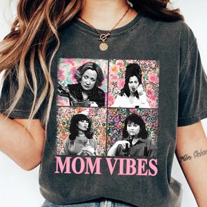 a woman wearing a black t-shirt with a graphic design of four photographs of a woman, along with the text "MOM VIBES" printed on the shirt.