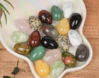 Puede incluir: Una colección de huevos de piedras preciosas pulidas en varios colores y patrones, incluyendo diseños rosas, verdes, negros y moteados. Los huevos están dispuestos en una fuente blanca, iridiscente, de forma ovalada, mostrando su belleza natural.