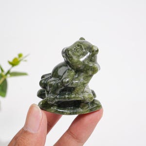 Könnte beinhalten: Eine kleine, handgeschnitzte Figur aus dunkelgrünem, gesprenkeltem Stein. Die Skulptur stellt ein stilisiertes Tier auf einem Sockel dar und zeichnet sich durch glatte, polierte Oberflächen mit sichtbarer natürlicher Maserung in Waldgrün aus.