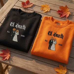 May include: A black sweatshirt and an orange sweatshirt, each featuring an embroidered graphic of a bride and groom with pumpkin heads. The text 'til Death' appears above the figures, with 'Est' on the left and '2026' on the right of the design.