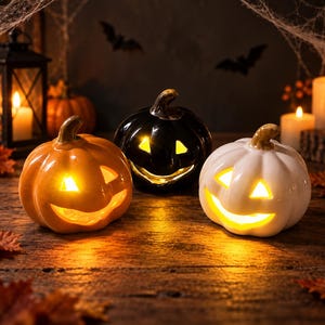 May include: Three ceramic jack-o'-lanterns in orange, black, and white, each featuring a carved face illuminated from within by a warm yellow light. The pumpkins have smooth, glossy surfaces and brown stems, arranged together as decorative items.