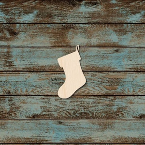 May include: A wooden Christmas stocking cutout, with a loop for hanging, set against a rustic, weathered blue and brown wood background. The stocking is a light beige color, perfect for holiday crafts and decorations.