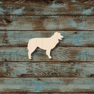 May include: A wooden cutout of a dog, likely a Collie or similar breed, standing in profile. The dog is light-colored, possibly unfinished wood, and is set against a backdrop of weathered, blue-toned wooden planks. The dog's features are simplified.