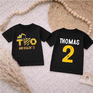 May include: Two black t-shirts. One shirt has a yellow excavator graphic with the word "TWO" and "AND DIGGIN' IT". The other shirt has the name "THOMAS" and the number "2" in yellow.