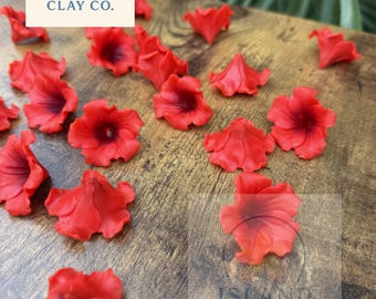 May include: Red clay flower petals scattered on a wooden surface. The petals have a dark red center and a lighter red edge. The Island Clay Co. logo is visible in the upper left corner.