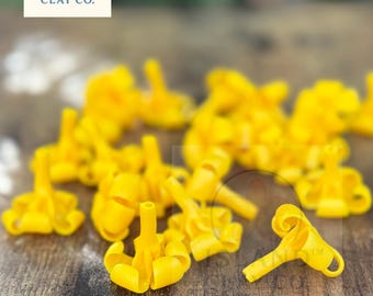 May include: Bright yellow clay pieces with a unique design are scattered on a wooden surface. The pieces have a central stem and curled edges. The Island Clay Co. logo is visible in the upper left corner.